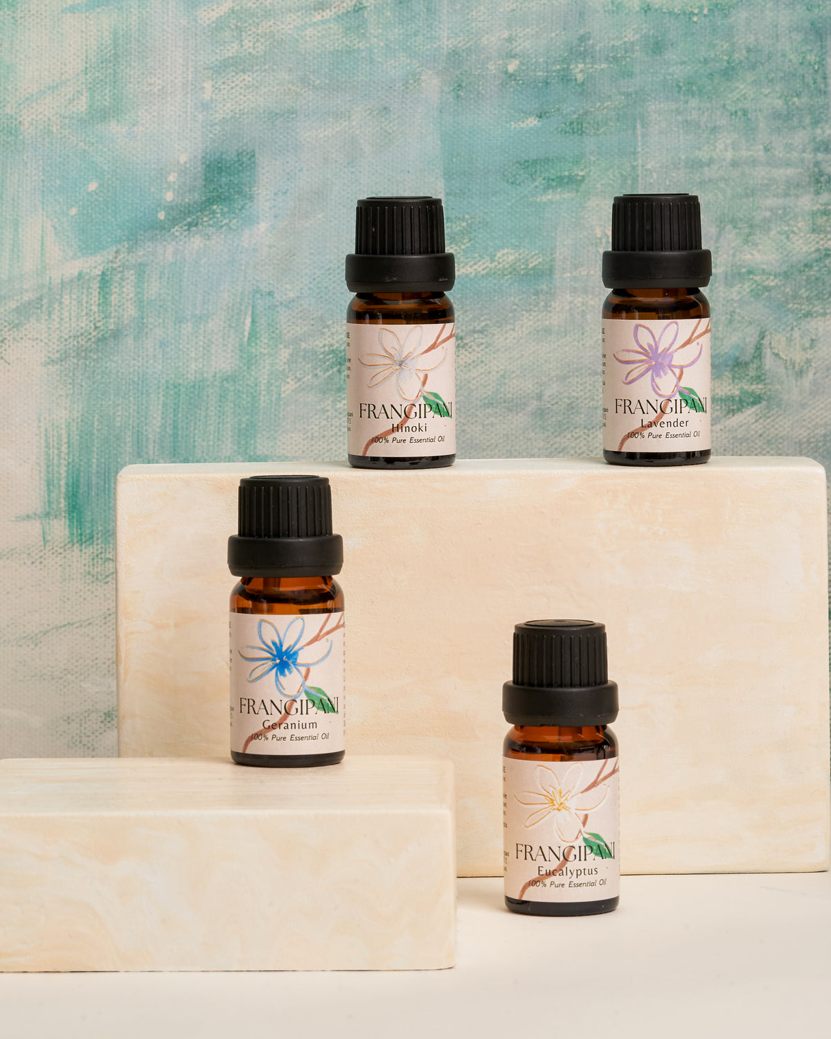 Four Frangipani essential oil bottles displayed on cream stone blocks