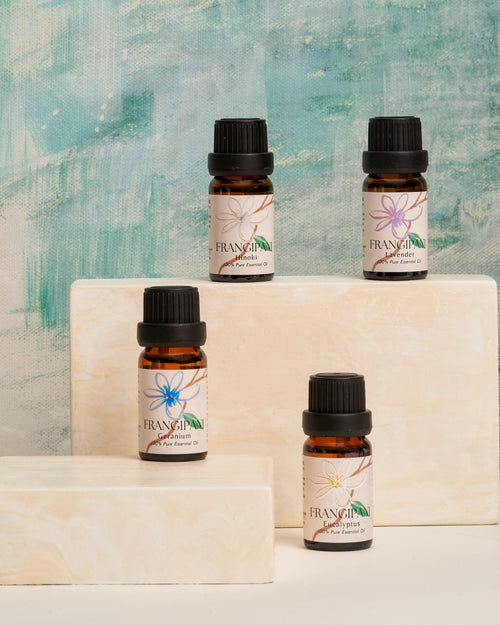 Four Frangipani essential oil bottles displayed on cream stone blocks