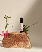 Frangipani Lavender & Hinoki roll-on atop a rock with a pink lily