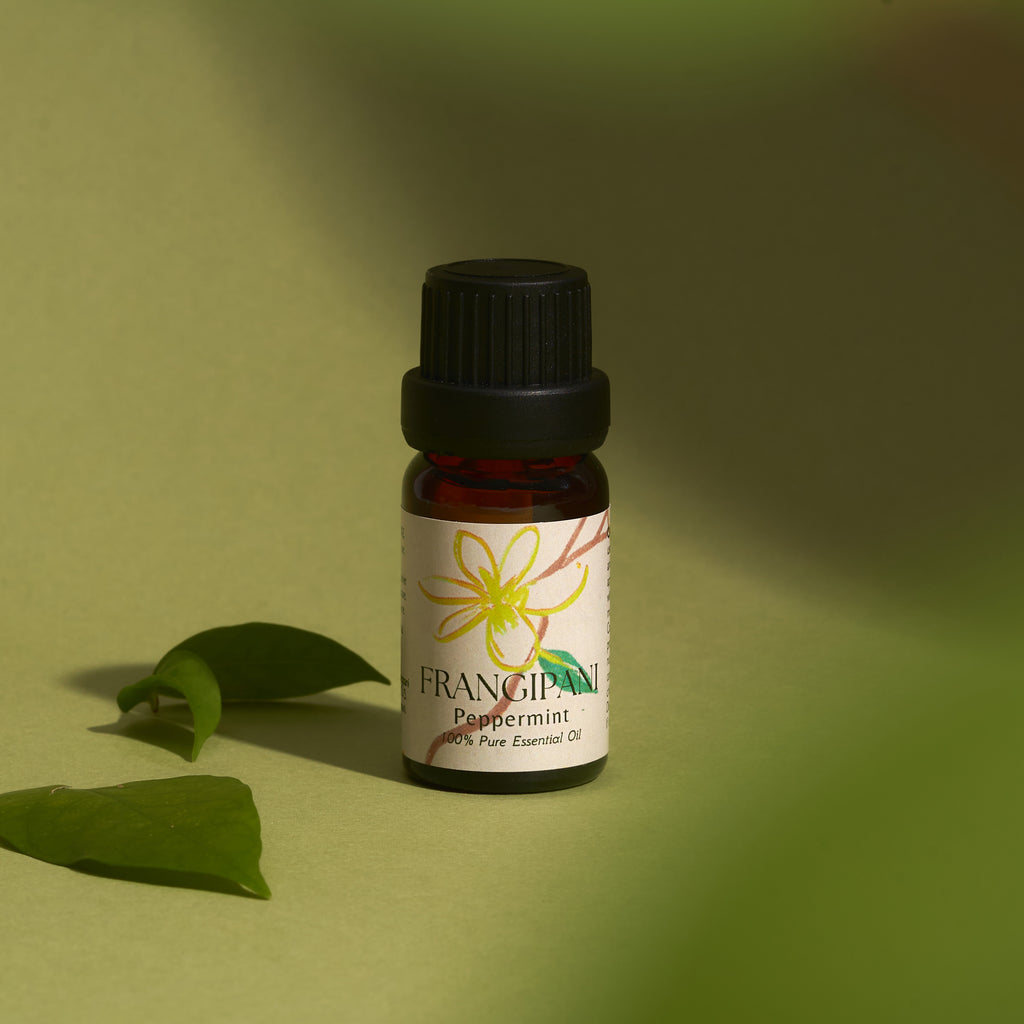 Frangipani Peppermint essential oil bottle with leaves on a green backdrop