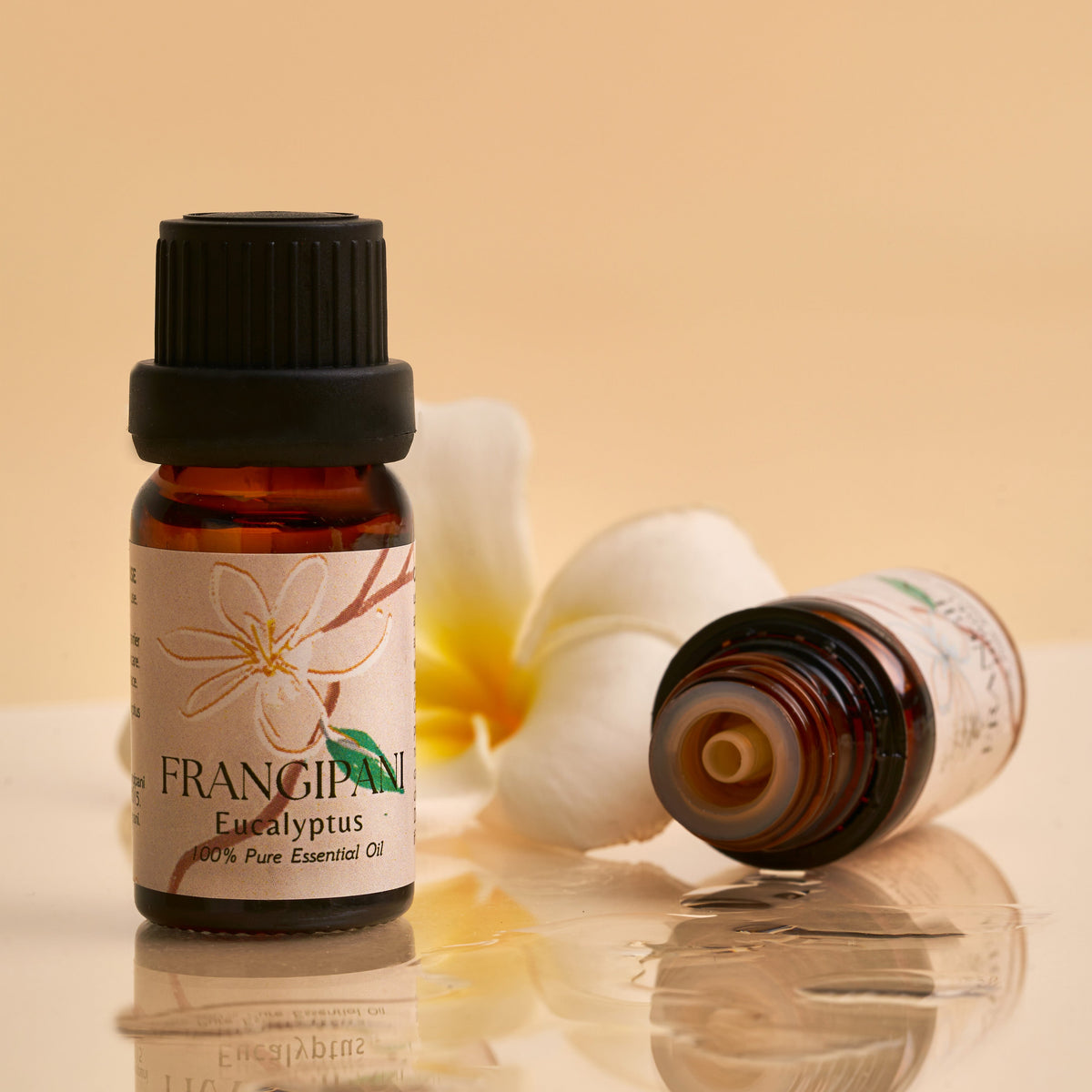 Frangipani Eucalyptus oil bottle upright beside an open bottle and plumeria