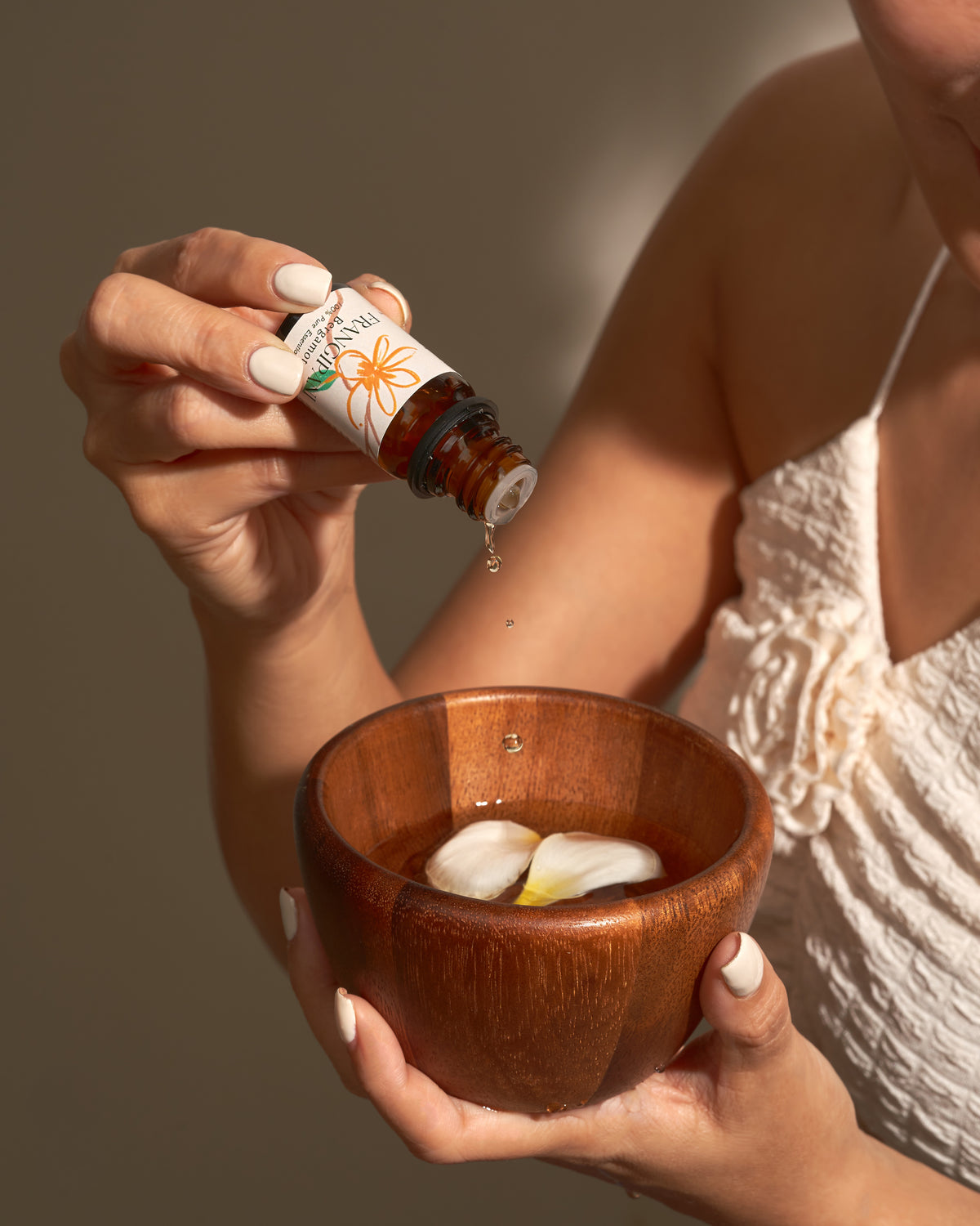 Frangipani Bergamot essential oil dripping into a wooden bowl of petals