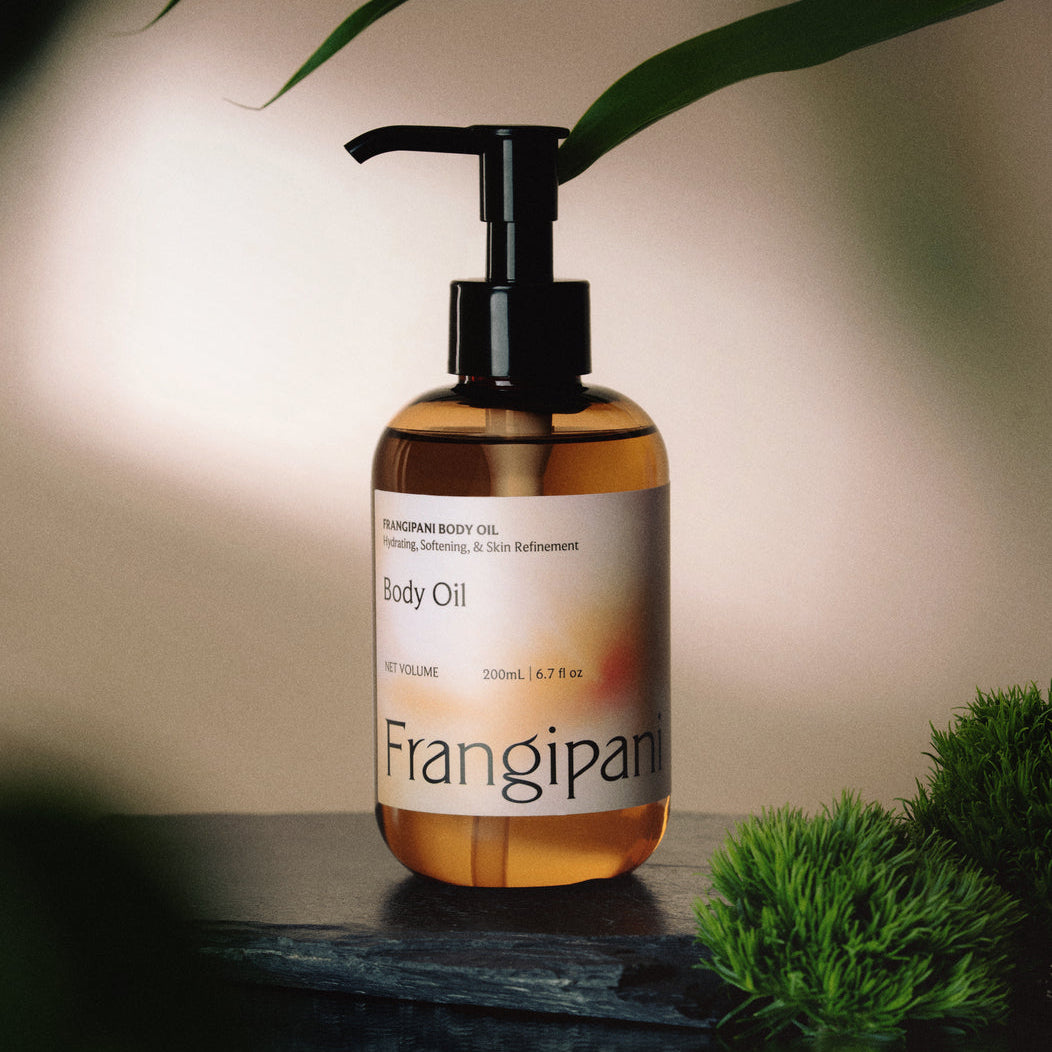Frangipani body oil pump bottle on dark slate with green moss