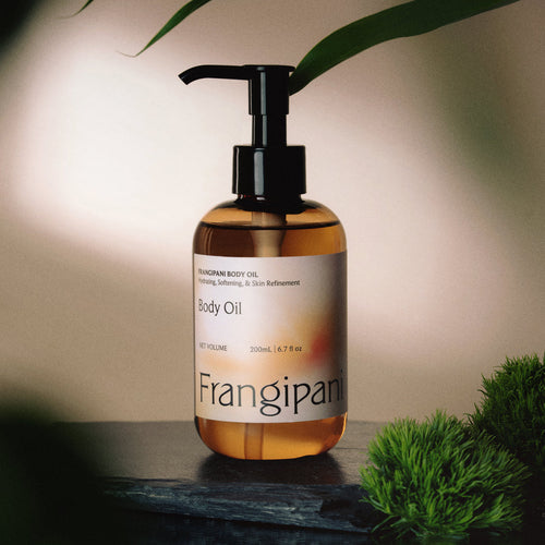Frangipani body oil pump bottle on dark slate with green moss