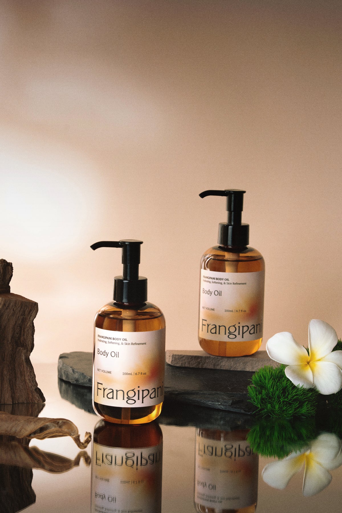 Two Frangipani body oil pump bottles staged with a white plumeria