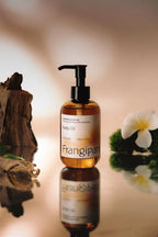 Frangipani body oil pump bottle reflected among driftwood and plumeria