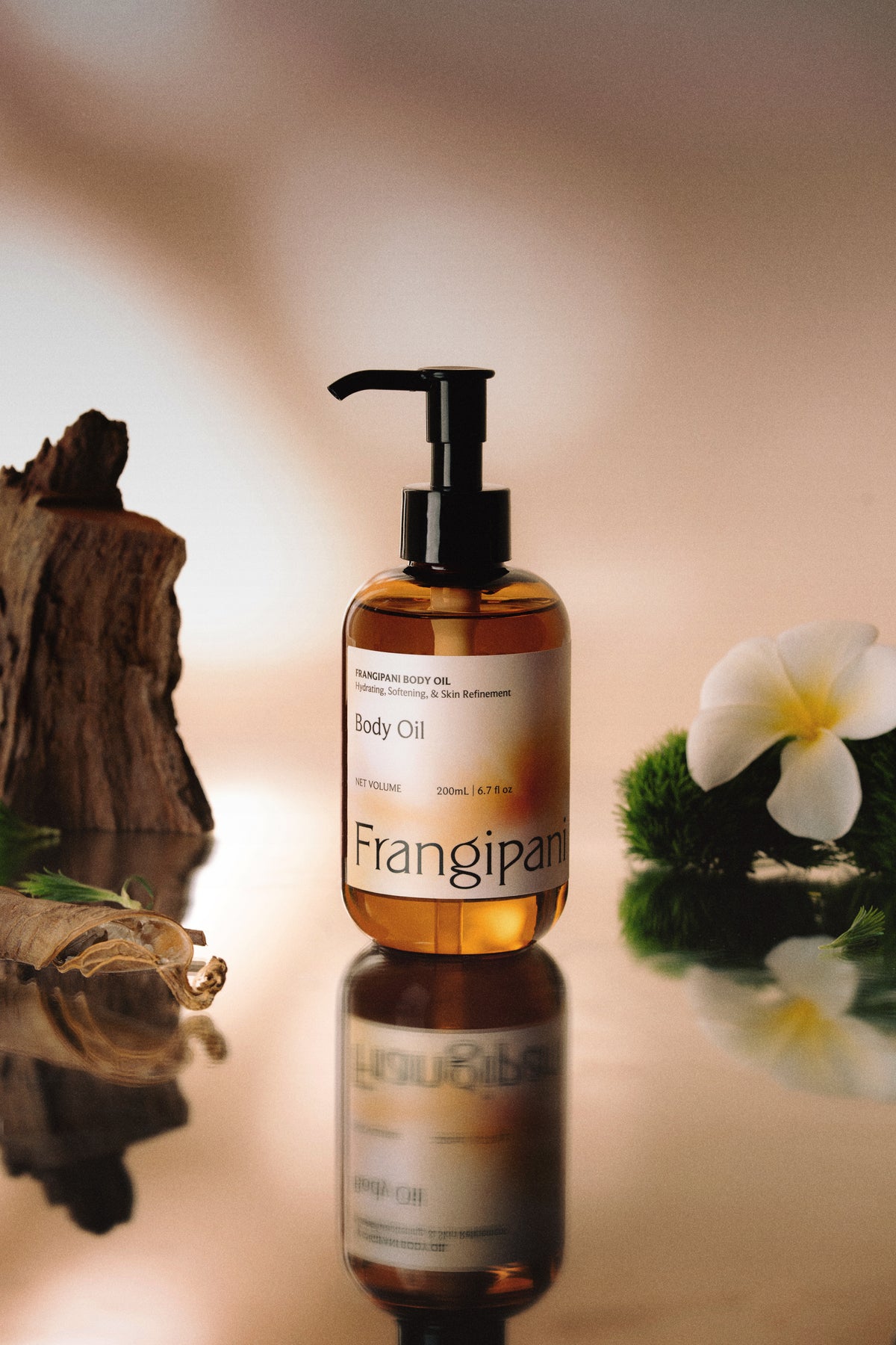 Frangipani body oil pump bottle reflected among driftwood and plumeria