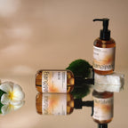 Two Frangipani body oil bottles with plumeria and moss on a reflective surface