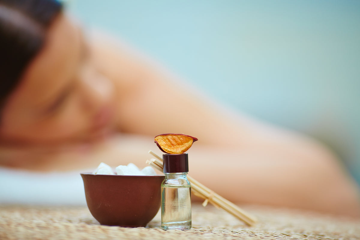 Woman receiving a massage with essential oils and a bowl of stones on a blurred background